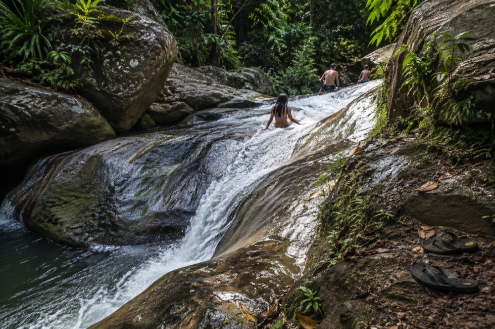 A narrow river chute of smooth rock running between boulders in the rainforest