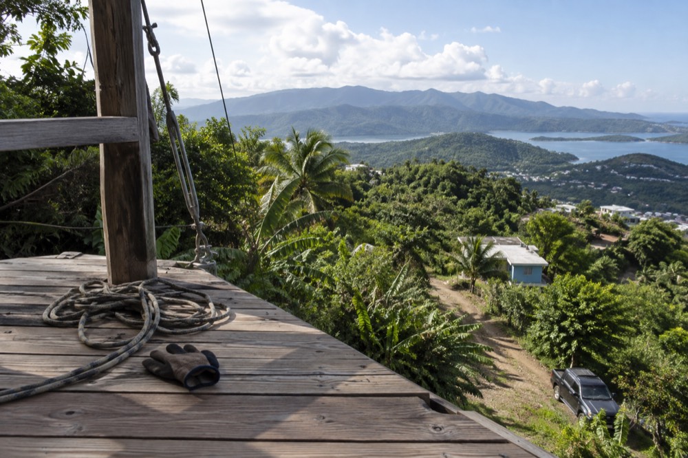 A zipline platform of wood and cable on a forested hillside overlooking green mountains