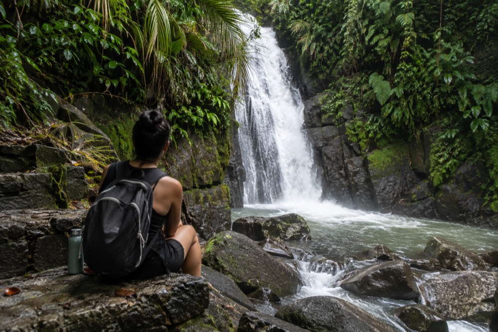 A hiker resting on a mossy stone step beside a rushing jungle stream