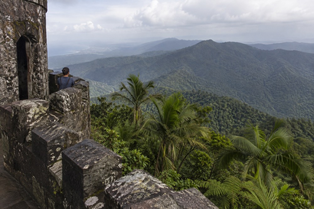 A stone observation tower overlooking layered green mountain ridges fading into haze