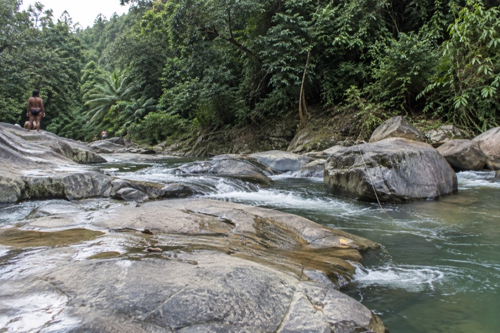 A shallow mountain river flowing over wide smooth bedrock in a green valley