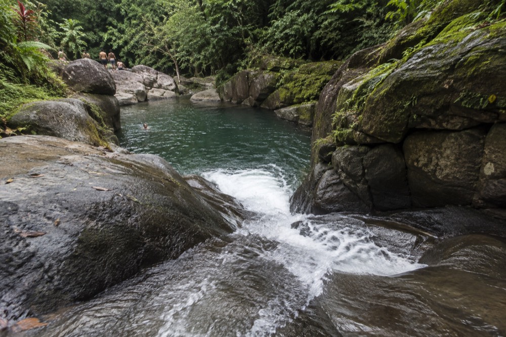Water rushing down a polished rock chute into a deep green pool at the base of a rock wall