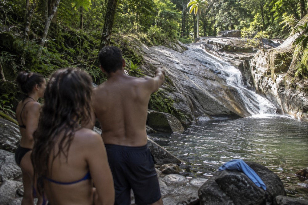 A guide pointing at a rock chute while a small group listens on the riverbank