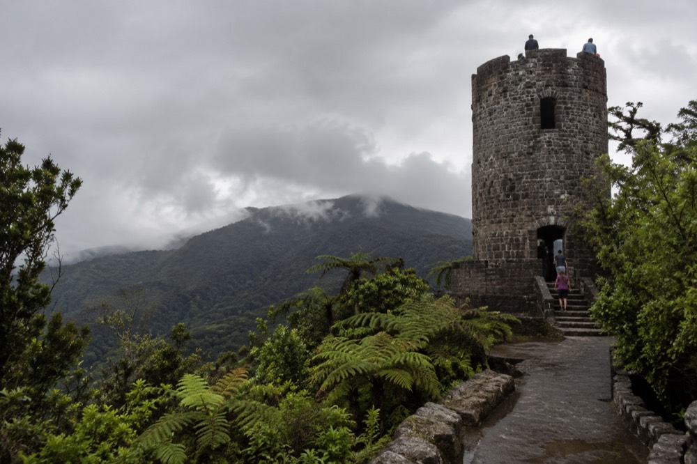 A stone observation tower rising above a lush green rainforest canopy under cloudy skies