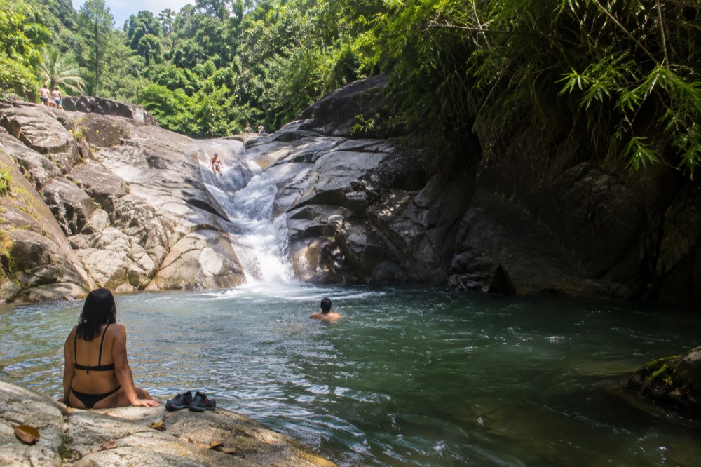 River pool at the base of a short waterfall surrounded by rocks and trees