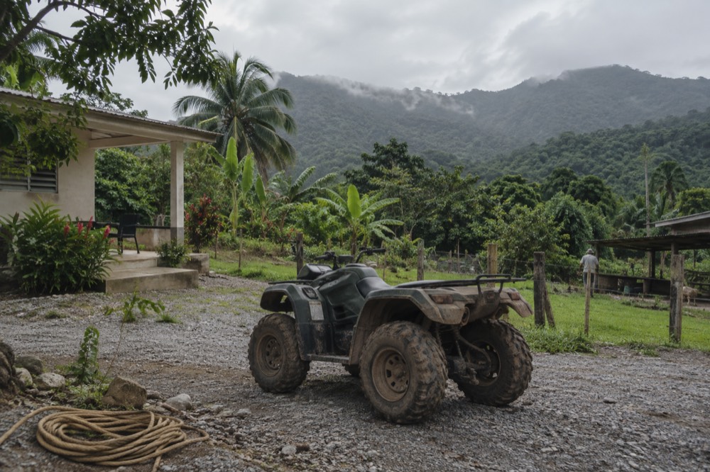 Riderless ATV parked on a gravel pad with rainforest hills in the background