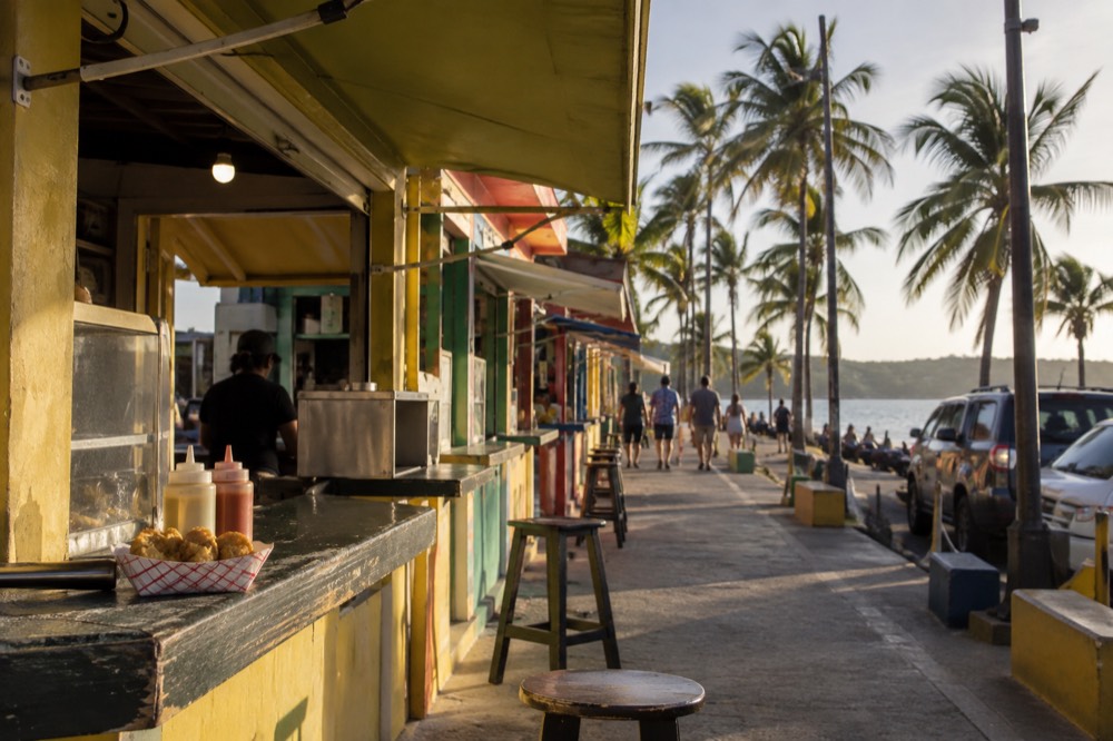 Food stalls with colorful signs along a beachfront row of kiosks