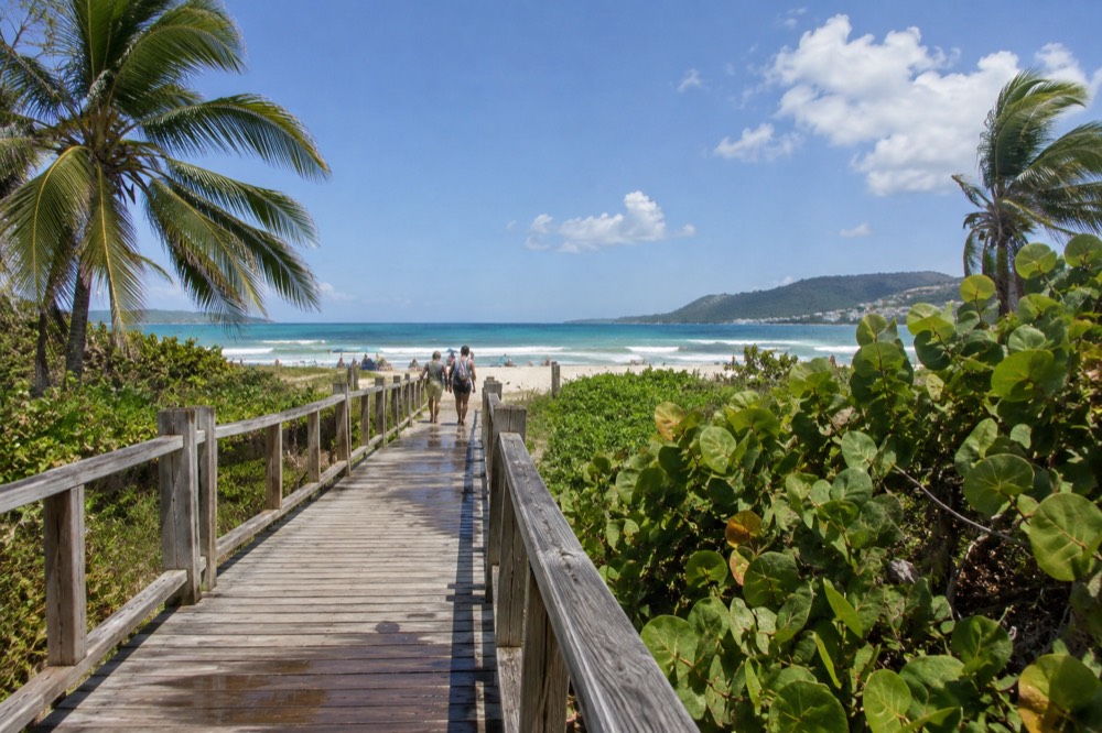 A long wooden pedestrian bridge crossing dunes toward a wide sandy beach