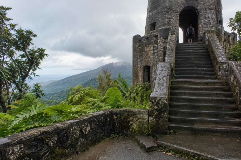 A stone observation tower overlooking layered green rainforest ridges under clouds