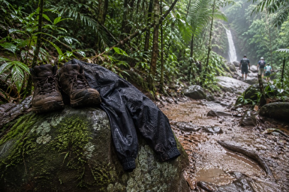Hiking boots and a rain jacket resting on a mossy rock beside a forest trail