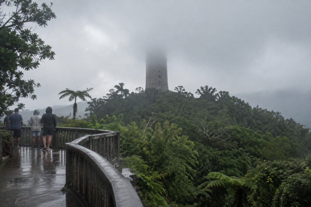 A stone observation tower rising above a rainforest ridge partly hidden by low clouds
