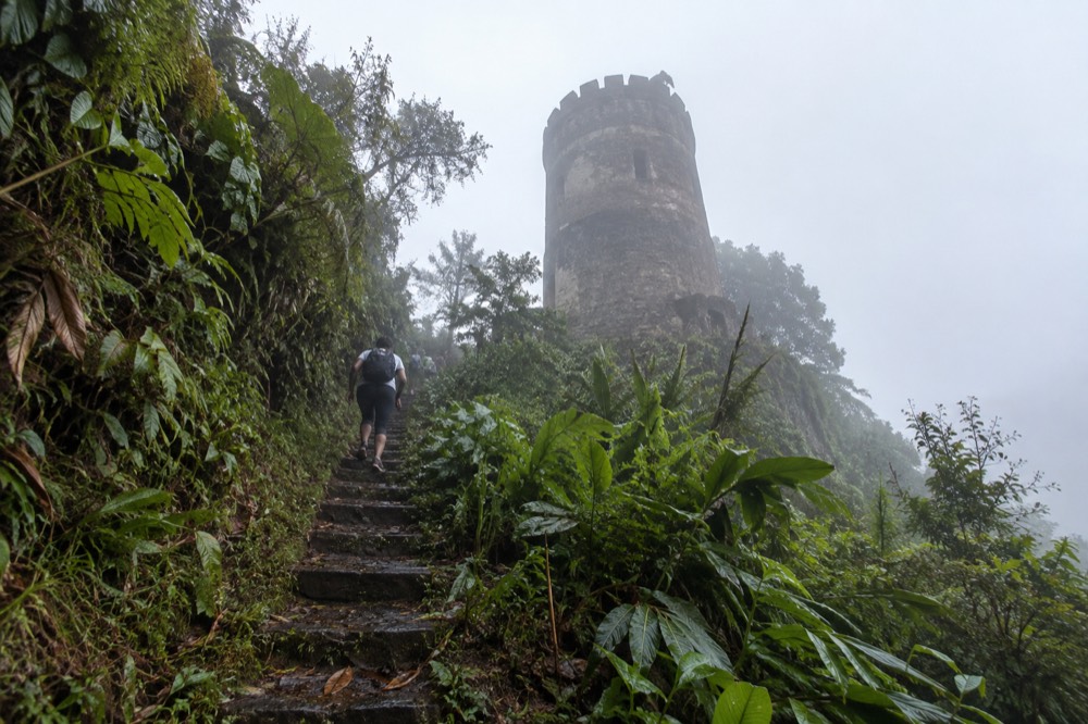 A round stone observation tower emerging from mist on a green mountain ridge