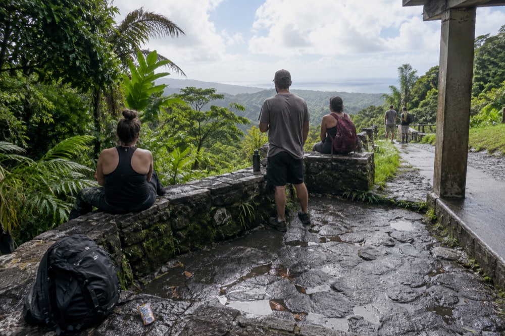 A small guided hiking group resting on a mossy stone platform above the treeline