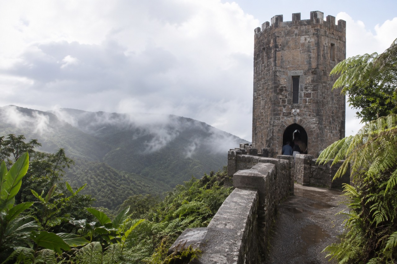 A stone observation tower on a forested mountain ridge above a sea of green clouds