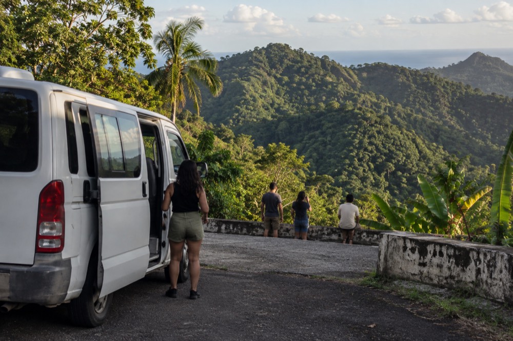 Small tour van parked at a roadside pullout overlooking green mountains