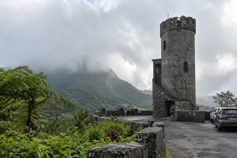 Stone observation tower on a forested ridge with clouds passing over green peaks