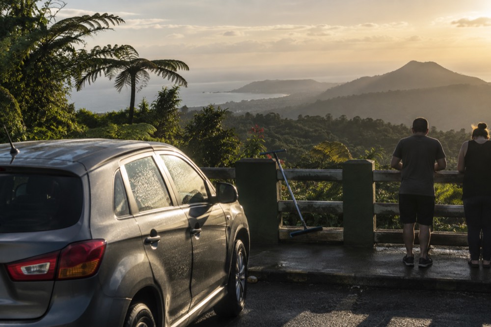 Car parked at a scenic overlook with a wide view of rainforest ridges and coastline