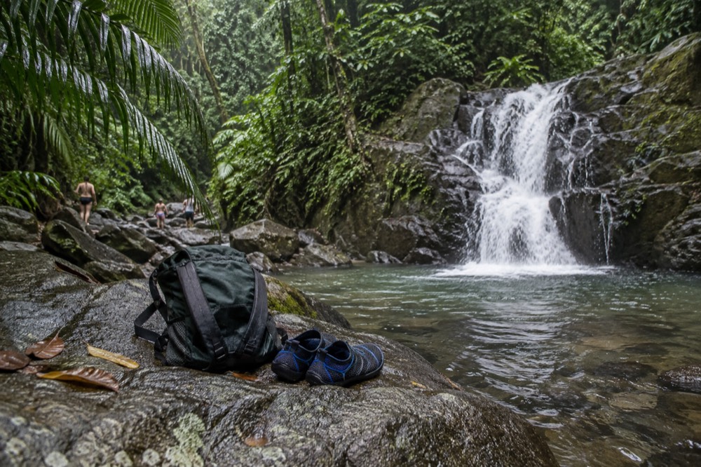 Backpack and water shoes resting on a wet rock beside a rainforest stream