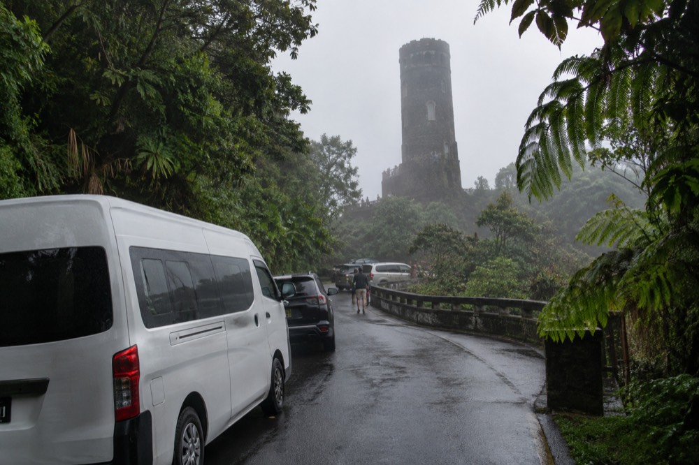 A tour van parked along a rainforest road with a tower in the distance
