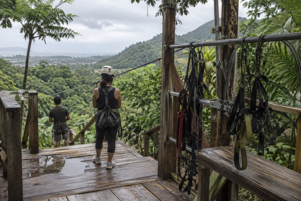 A wooden zipline platform with coiled cables and harnesses hanging from a rail