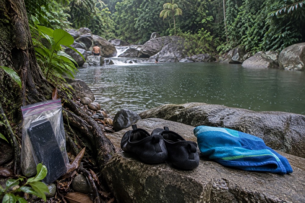 A pair of water shoes and a folded towel on a rock beside a forest stream