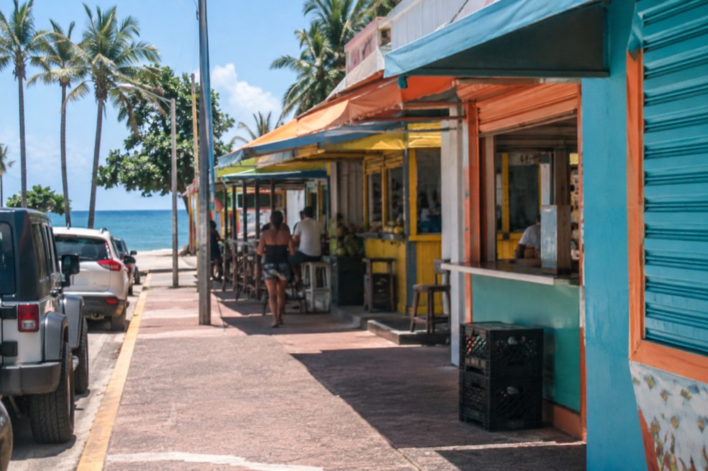 Colorful painted kiosk storefronts with hand-lettered signs along a coastal street