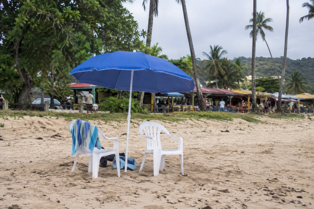 Beach umbrella and chairs on sand with food stalls visible in the background