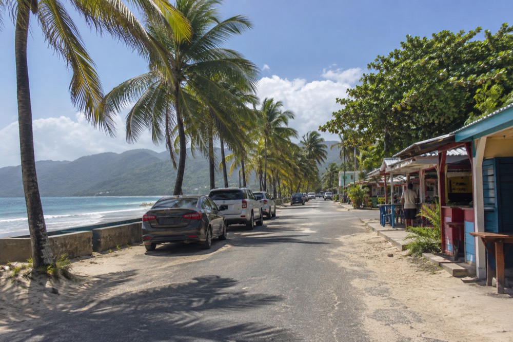 Palm-lined coastal road with parked cars and food stalls along the waterfront