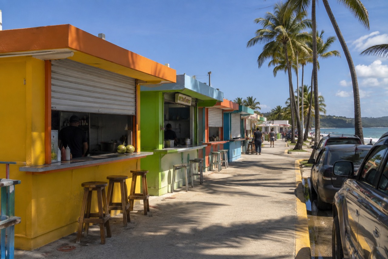 Row of colorful food kiosks along the Luquillo shoreline under a blue sky