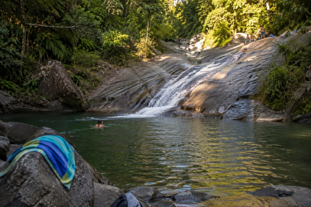 A calm river pool at the base of a rock slide, ringed by trees