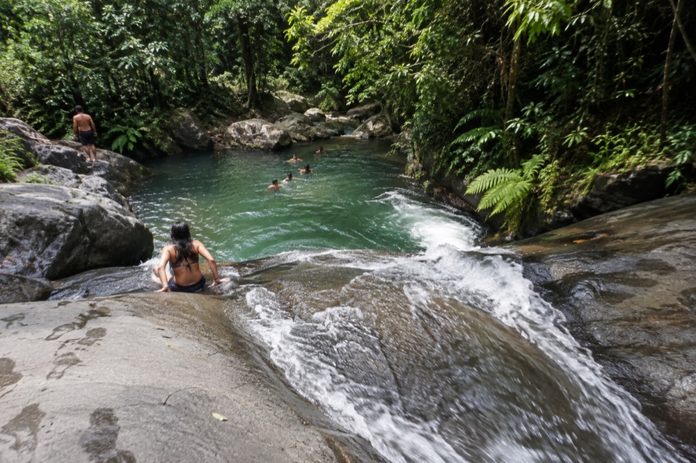 A natural rock waterslide with water running down smooth stone into a forest pool