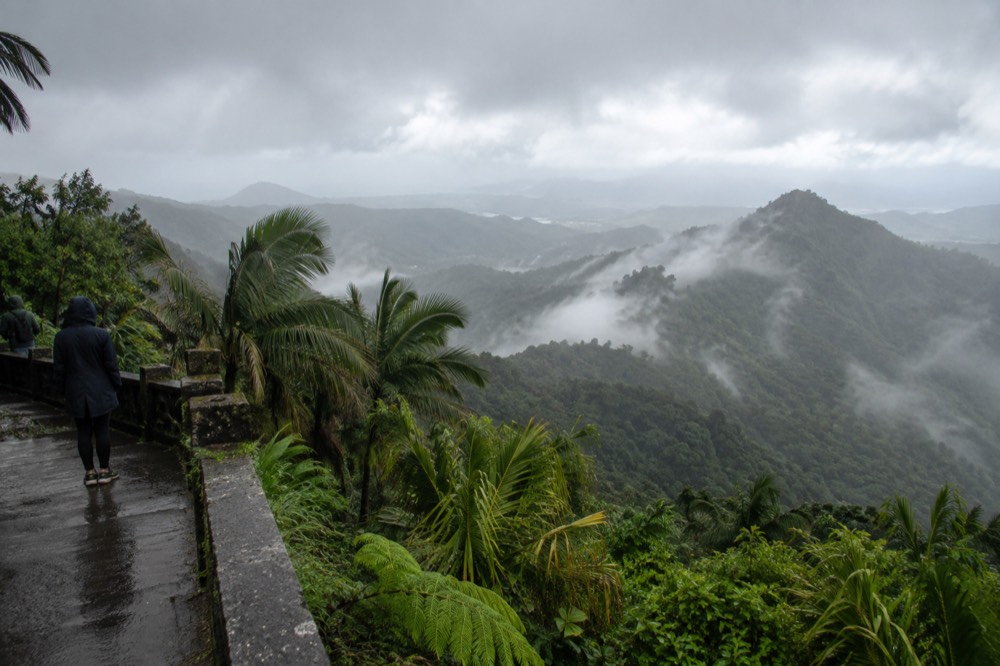 Rain mist drifting through layered green mountain ridges under a grey tropical sky