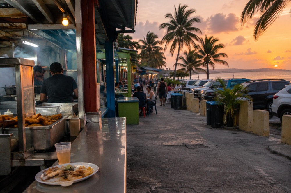 Colorful beachside food kiosks along a coastal road with palm trees