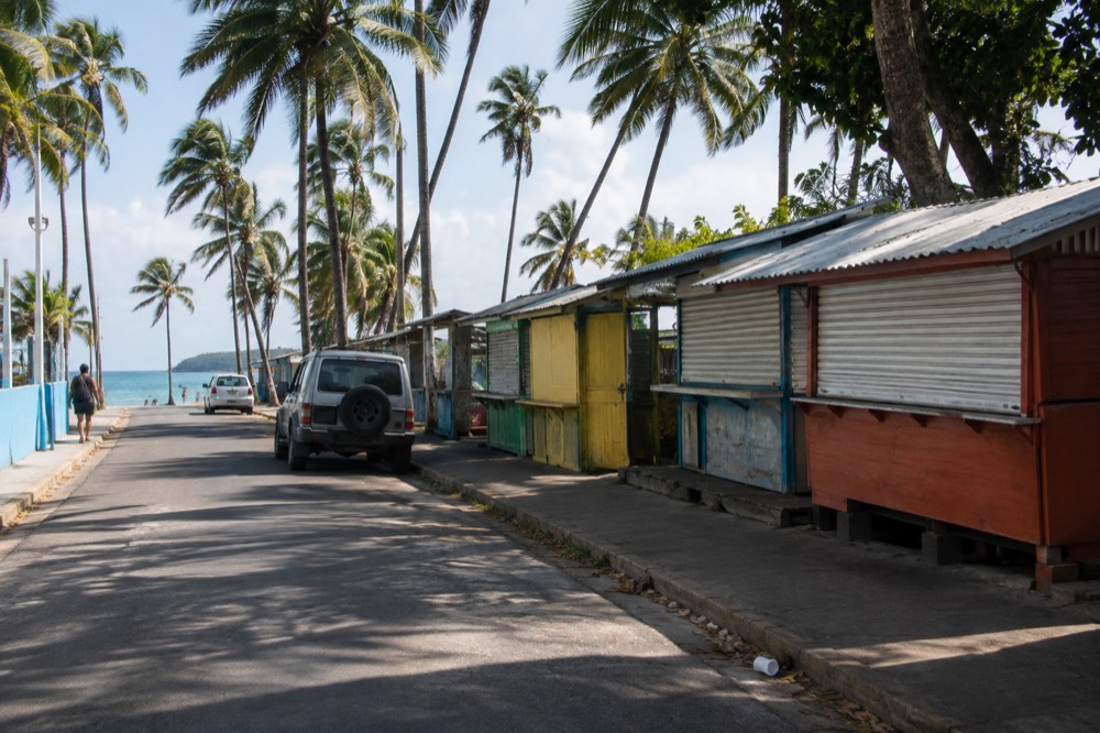 A small beach town road with palm trees and a line of food kiosk stalls under bright afternoon sun