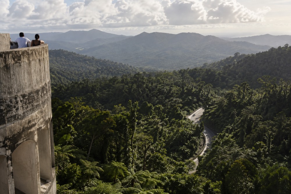 Rooftop viewpoint over a green mountain valley with road winding through trees