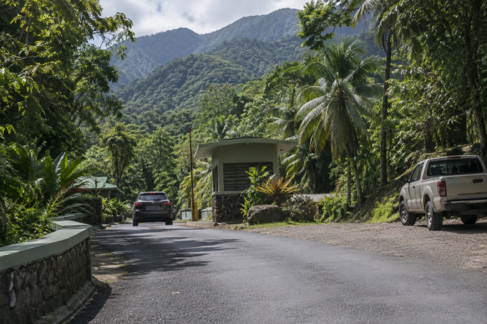 Sign and road at a tropical forest entrance with mountains behind